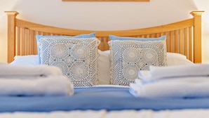 Una cama bien hecha con cabecera de madera, dos almohadas estampadas y un cuadro enmarcado encima.