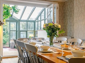 A dining area with a table set for four, surrounded by chairs, with a large window providing a view of greenery outside. - 6 Bed in Winchelsea (oc-77281) (Icklesham)