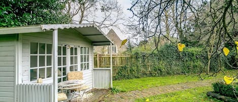 En liten, vit träbyggnad med en veranda, en gång av tegelstenar och en gräsplätt.