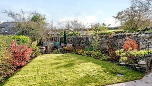 Ein gepflegter Garten mit einer Steinmauer, einem Kiosk und verschiedenen Pflanzen.