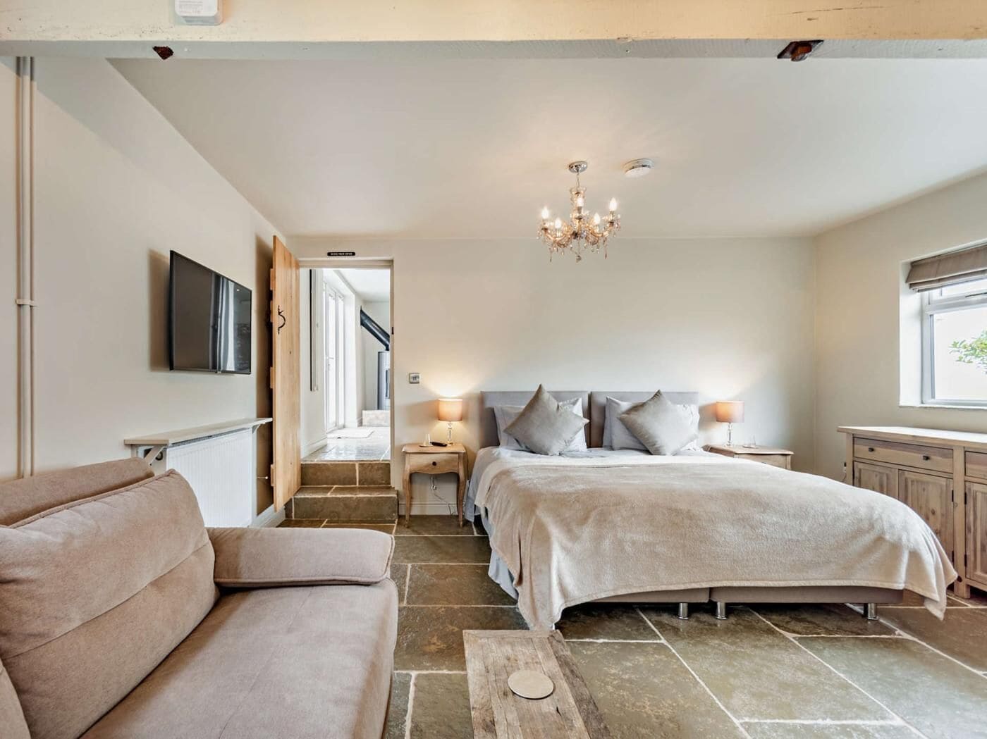 A bedroom with a bed, bedside tables, a TV, a chandelier, and a window.