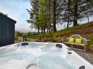 Ein Whirlpool mit einer hölzernen Sitzbank und Kissen, umgeben von Bäumen und einer Steinmauer.