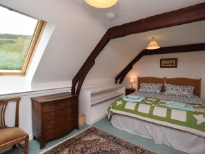 A bedroom with a sloped ceiling, a bed with patterned bedding, a wooden dresser, a chair, and a window with a view of greenery. - 2 Bed in Biggar (oc-ca366) (Biggar)