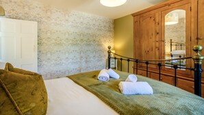 Quarto com cama, guarda-roupa de madeira, espelho e parede estampada.