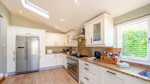 A modern kitchen with white cabinets, stainless steel appliances, and a window with blinds.