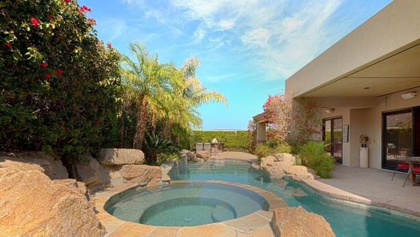 A swimming pool with a hot tub, surrounded by rocks and plants, with a building and patio area in the background. - 5 BR Custom Mediterranean Estate In Andreas Hills, 5 King Beds Putting Green... (Palm Springs)