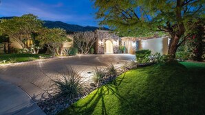 A well-lit driveway leading to a stone building with an arched entrance, surrounded by landscaped gardens and trees. - 5 BR Custom Mediterranean Estate In Andreas Hills, 5 King Beds Putting Green... (Palm Springs)