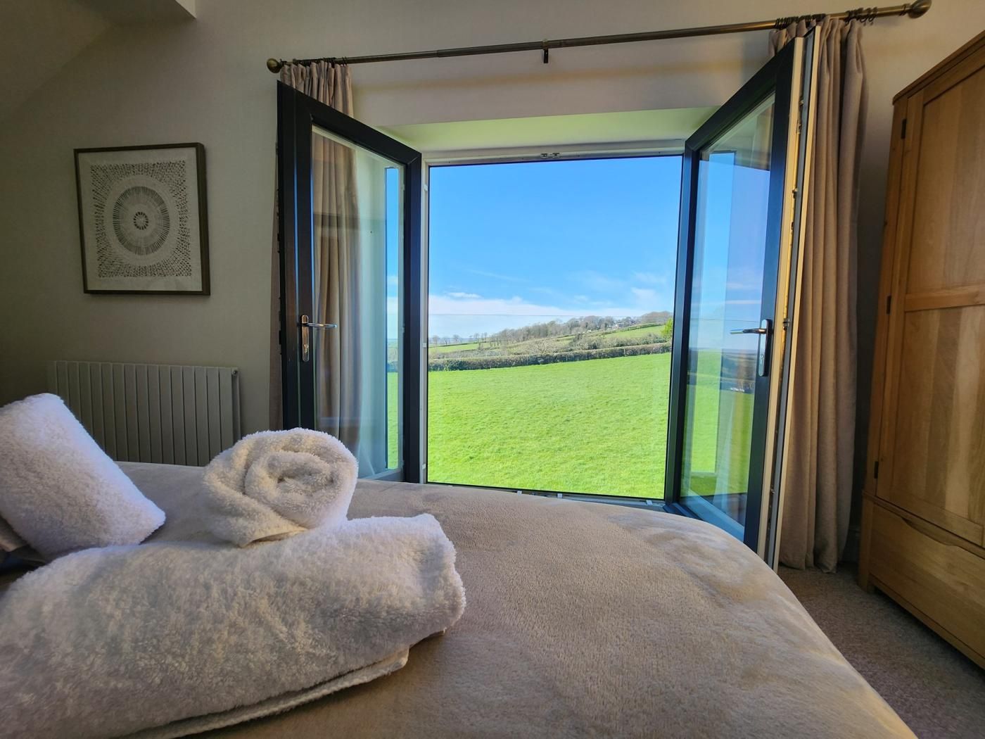 Ein Schlafzimmer mit einem großen Bett, Blick auf ein grünes Feld durch eine offene Tür und einem Heizkörper an der Wand.