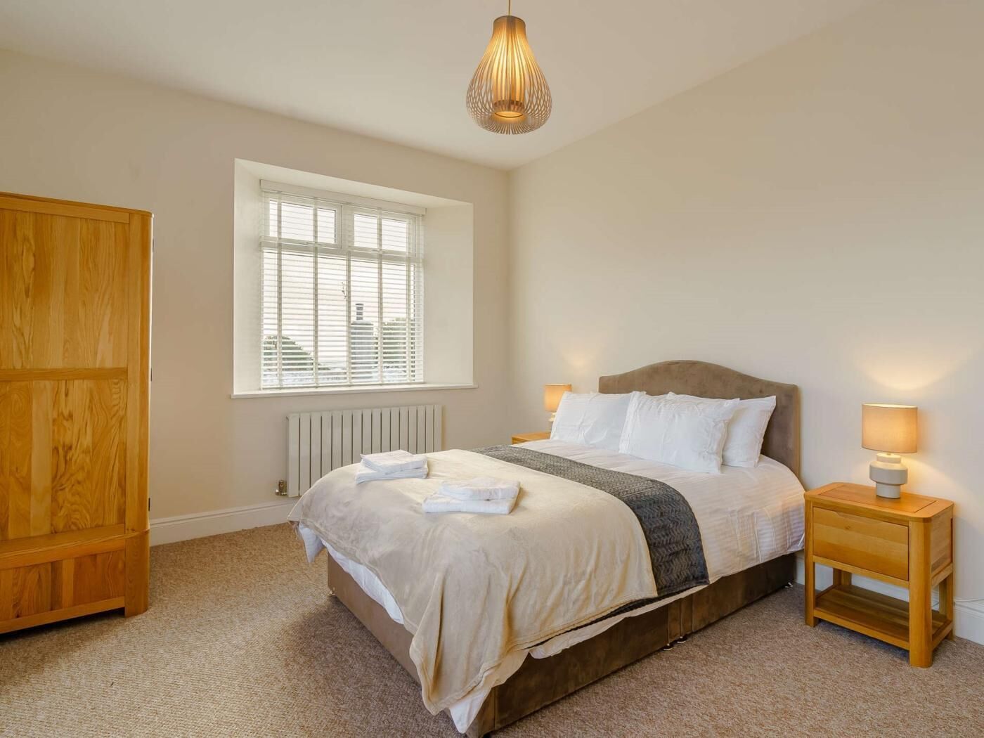 A bedroom with a bed, a window, a radiator, a wardrobe, and a bedside table with a lamp.