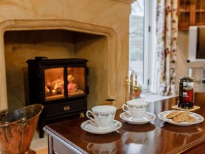 A cozy room with a fireplace, a wooden table with tea cups and a plate of cookies, and a copper bucket. - 1 Bed in Chard (oc-91135) (Chaffcombe)
