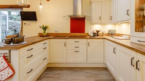 Une cuisine avec des meubles blancs, un plan de travail en bois, une hotte de cuisinière en acier inoxydable et un puits de lumière.