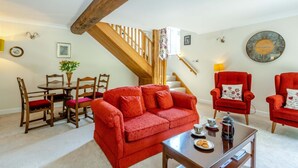 Un salon avec un canapé rouge, une table à manger en bois, des chaises, un escalier et un fauteuil rouge.