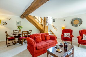 Ein Wohnzimmer mit einem roten Sofa, einem Holzesstisch, Stühlen, einer Treppe und einem roten Sessel.