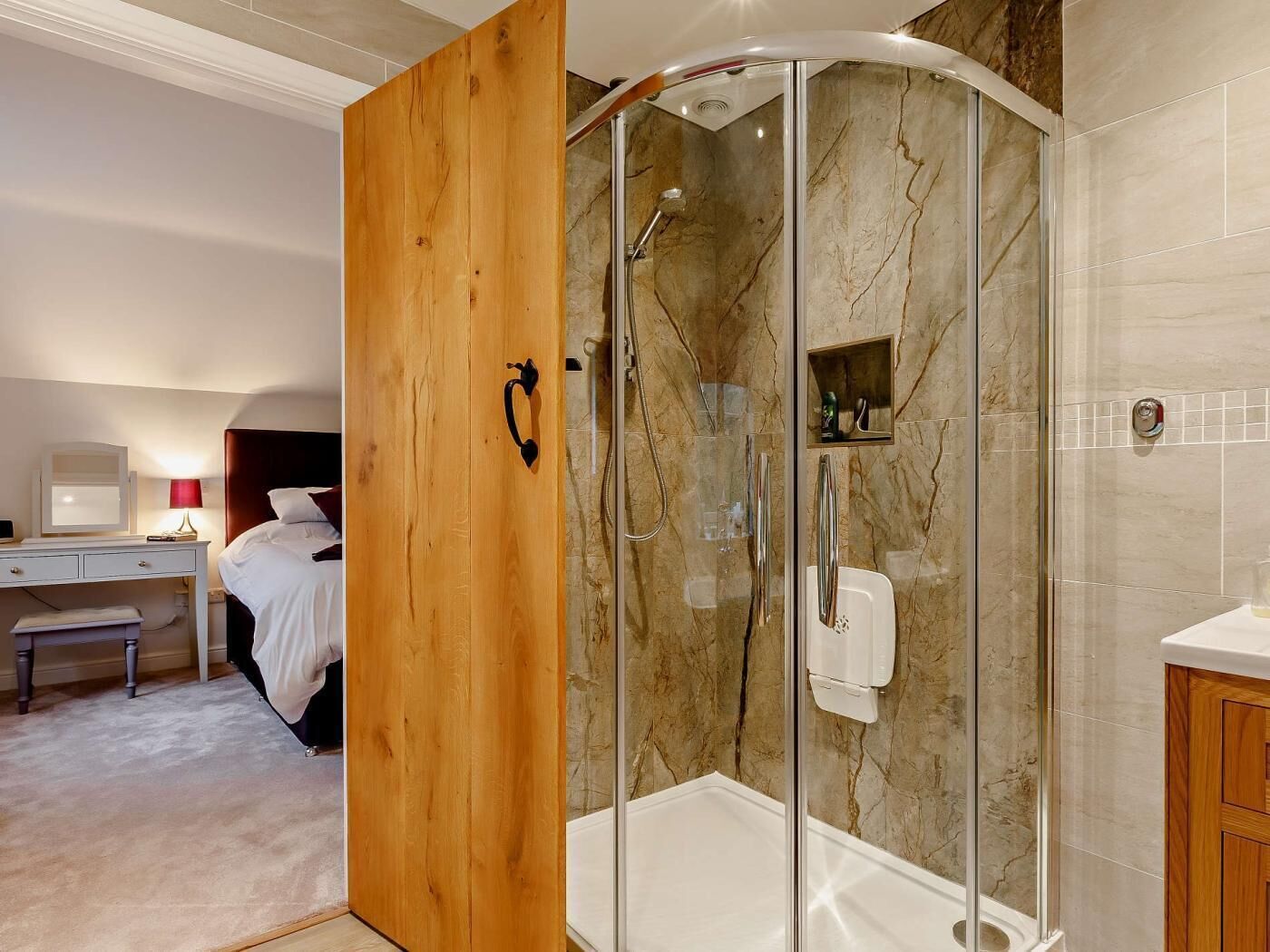 A modern bathroom with a glass-enclosed shower, marble walls, and a wooden door.