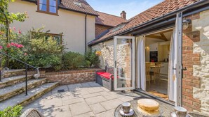 Une terrasse avec une table et des chaises, un banc rouge et une porte vitrée donnant sur un espace cuisine.