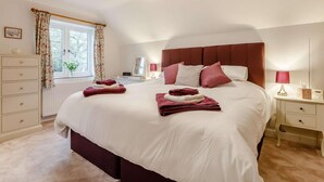 Une chambre à coucher avec un grand lit, des tables de chevet, une commode, une fenêtre avec des rideaux et un luminaire au plafond.