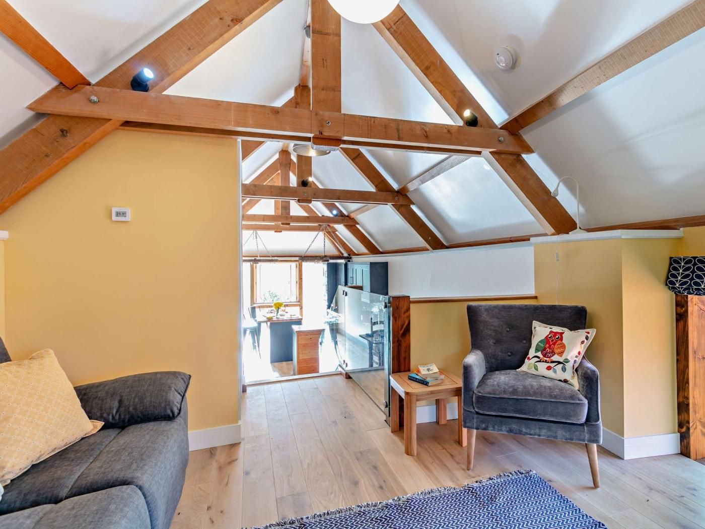 Ein geräumiges Loft mit freiliegenden Holzbalken, einem grauen Sofa, einem kleinen Tisch und einem Stuhl mit einem Zierkissen.