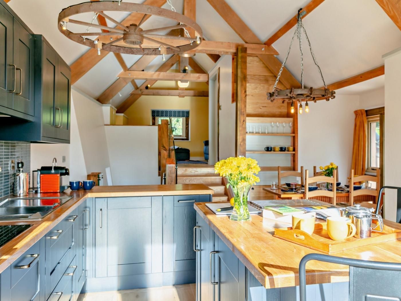 A kitchen with a wooden ceiling, a central island with a vase of flowers, and a dining area with wooden chairs and a table.