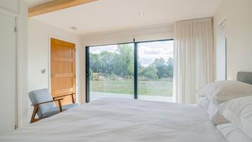 Une chambre avec un grand lit, une chaise, une porte en bois et une vue sur un espace verdoyant, visible à travers une porte-fenêtre coulissante.