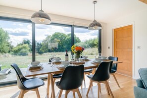 Un coin repas avec une table dressée pour six personnes, de grandes fenêtres et une vue sur l’extérieur.