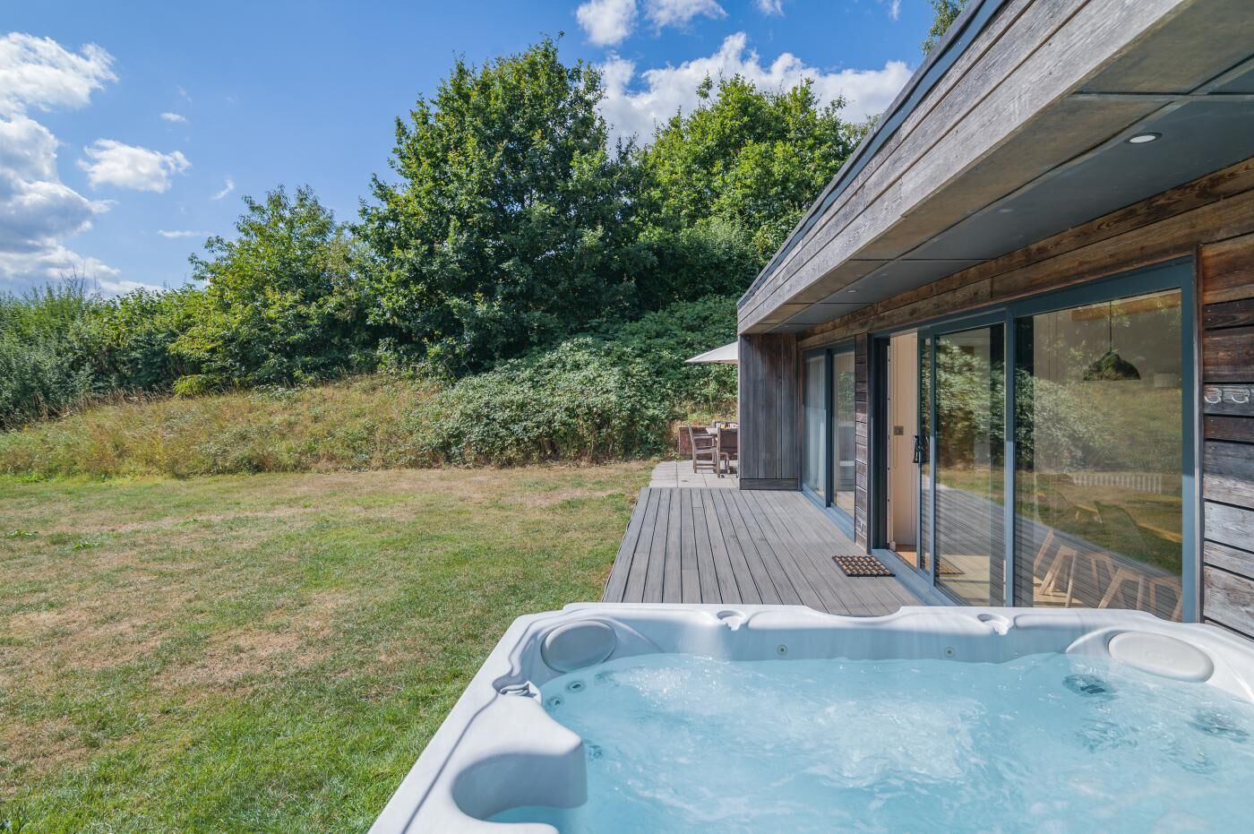 A hot tub on a wooden deck with a view of a house and surrounding greenery.