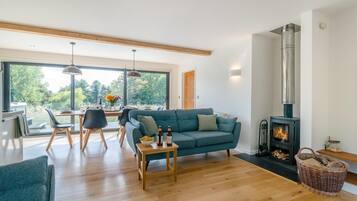 A modern living room with a sofa, dining table, and a wood-burning stove.