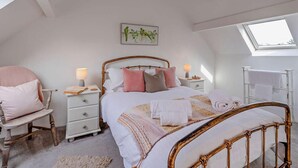 Ein Schlafzimmer mit Bett, Nachttischen, einem Sessel, einem Fenster und einem Dachfenster.