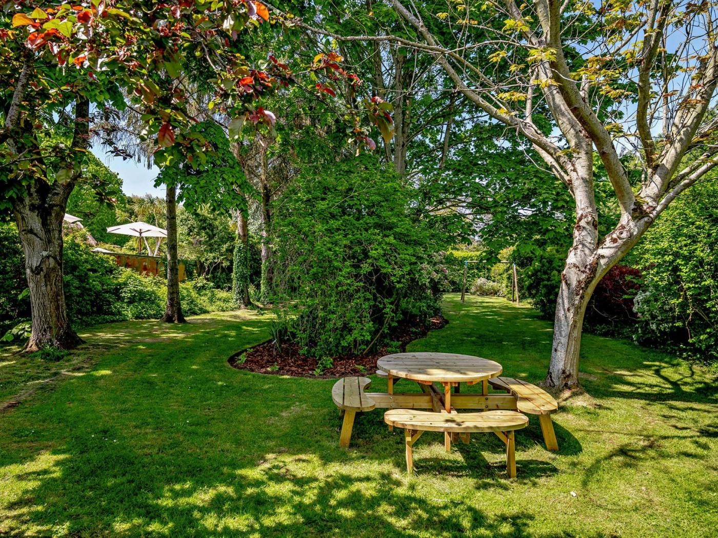 A garden with a wooden table and benches, surrounded by trees and greenery.