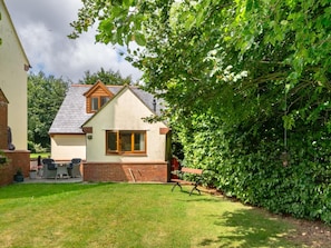 A two-story house with a sloped roof, a front porch with a bench, and a well-maintained lawn. - 1 Bed in Taunton (oc-ndown) (Otterford)