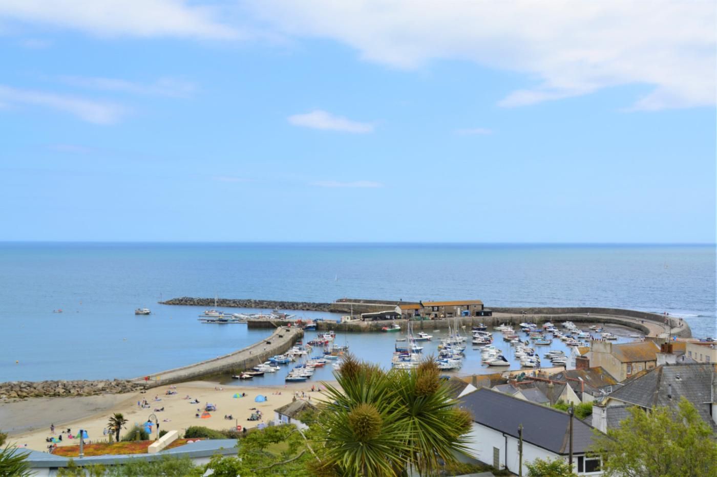 Un pueblo costero con un puerto deportivo, playa de arena y edificios a lo largo del paseo marítimo.
