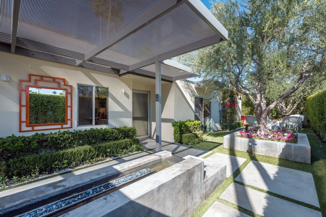 Une maison moderne dotée d’un patio couvert, d’un petit jardin avec un arbre et d’un cadre de fenêtre décoratif.