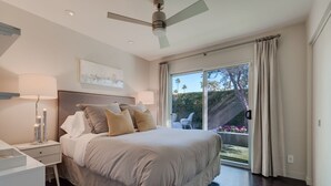 Ein Schlafzimmer mit einem Bett, Nachttischen, einem Deckenventilator und Blick auf einen Garten durch eine Schiebetür.