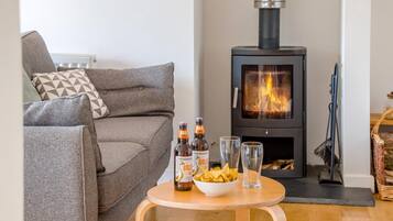 A cozy living room with a sofa, a table with snacks and drinks, and a wood-burning stove.