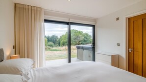 Habitación de hotel con una cama grande, una puerta de madera y vistas a un jardín a través de una puerta corrediza de vidrio.