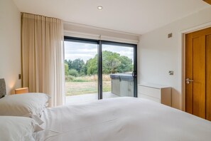 A hotel room with a large bed, a wooden door, and a view of a garden through a sliding glass door.