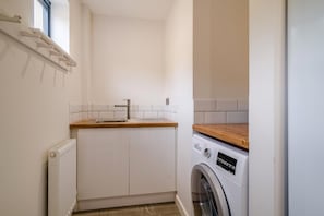 A compact laundry room with a built-in washing machine, a sink, and a wooden countertop.