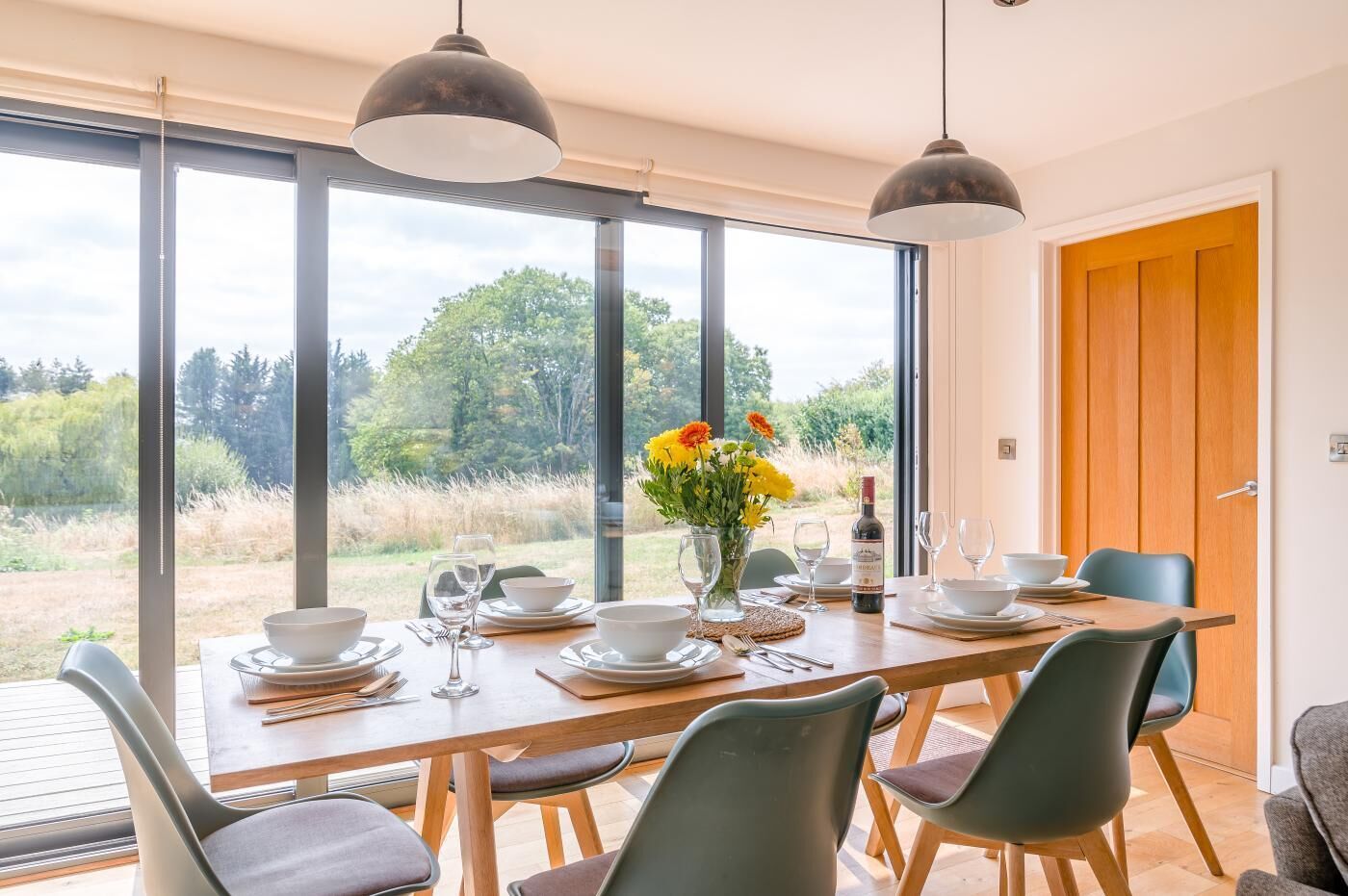 Un coin repas avec une table dressée pour quatre personnes, de grandes fenêtres et une vue sur l’extérieur.