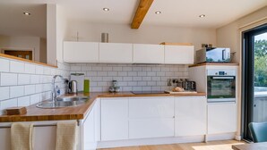 Una cocina moderna con armarios blancos, encimera de madera, un fregadero, un hervidor y un horno.