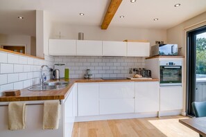 A modern kitchen with white cabinets, a wooden countertop, a sink, a kettle, and an oven.