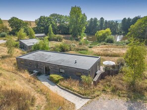 A modern building with a flat roof, surrounded by natural landscape and a body of water.