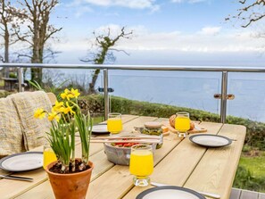 A wooden table set with plates, glasses, and a potted plant, overlooking a body of water. - 2 Bed in Taunton (oc-87641) (West Quantoxhead)