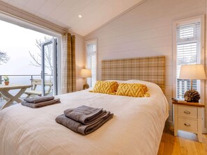 A hotel room with a bed, a nightstand, a window with blinds, a view of the outdoors, and a wooden table with chairs. - 2 Bed in Taunton (oc-87641) (West Quantoxhead)