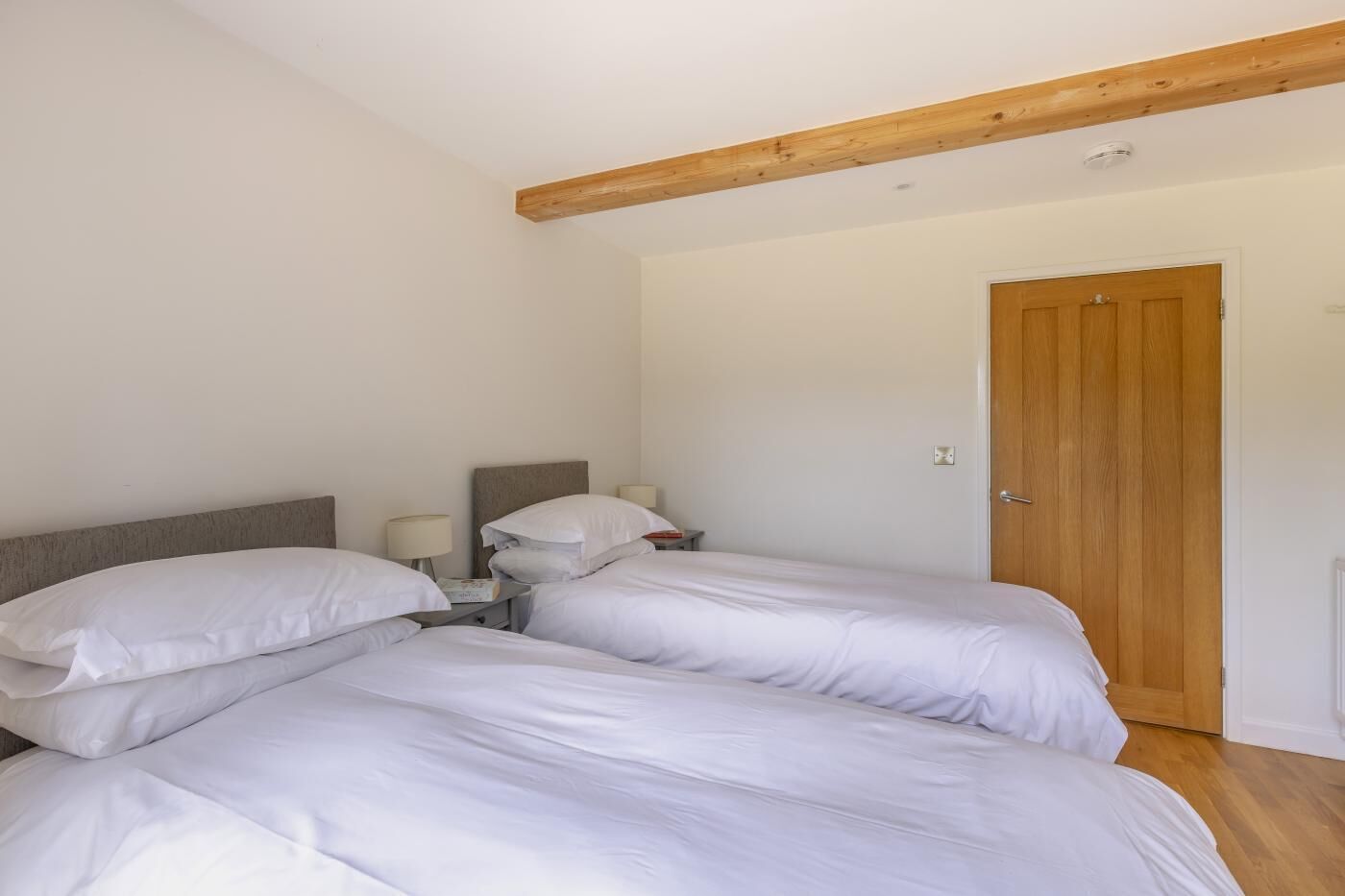 Una camera da letto con due letti, un trave in legno al soffitto, una porta e un comodino con una lampada.