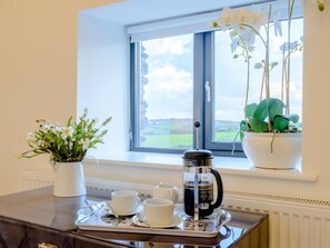 Ein Zimmer mit Fenster, einem Tisch mit Tablett, Kaffeemaschine, Tassen und einer Topfpflanze.