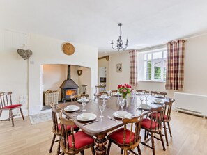 Comedor con una mesa grande dispuesta para seis personas, sillas de madera con cojines rojos, chimenea y una ventana con cortinas.