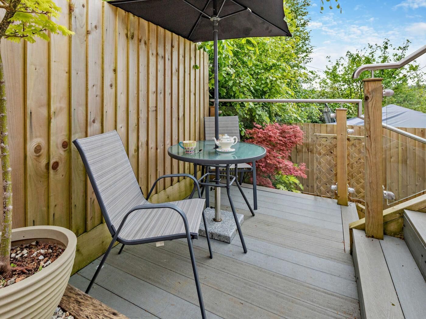A wooden deck with a table and chairs, a potted plant, and a wooden fence.