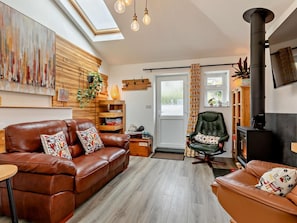A cozy living room with a brown leather sofa, a green chair, a fireplace, and a skylight. - 2 Bed in Barnstaple (oc-94038) (Bishop's Tawton)