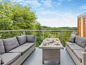 A balcony with wicker furniture, a table set for tea, and a scenic view of green hills. - 2 Bed in Barnstaple (oc-94038) (Bishop's Tawton)