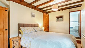 Ein Schlafzimmer mit einem Holz-Kopfteil, einem Bett mit Blumenmuster-Bettwäsche, einem Nachttisch, einem Holzschrank und einem durch eine offene Tür einsehbaren Badezimmer.