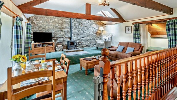 Ein gemütliches Wohnzimmer mit Steinwand, Holzbalken, Kamin, einer Couch, einem Fernseher und einem Essbereich mit Tisch für zwei Personen.